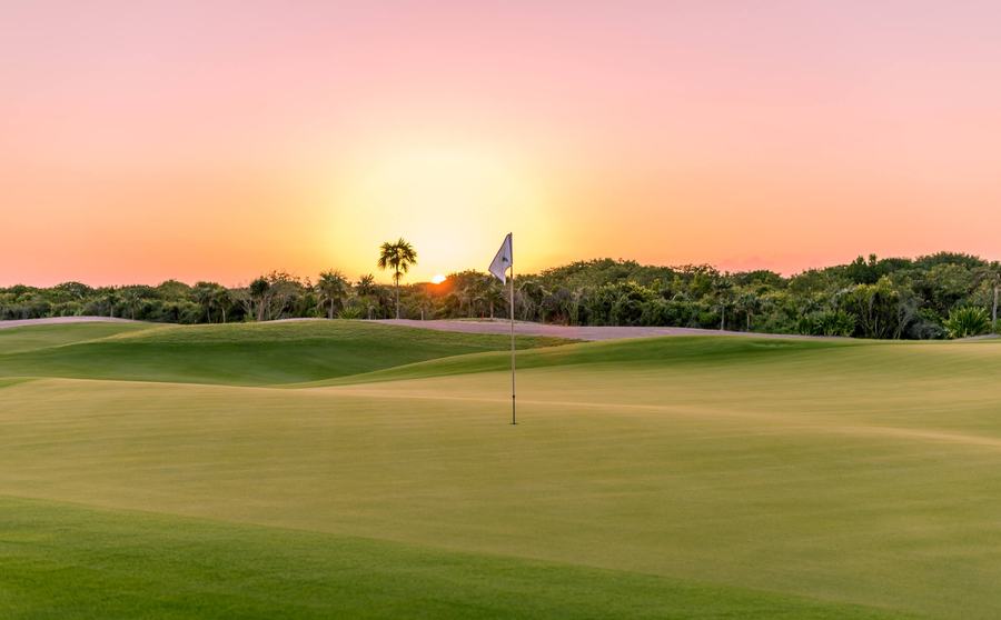 A golf hole with a flag at sunset
